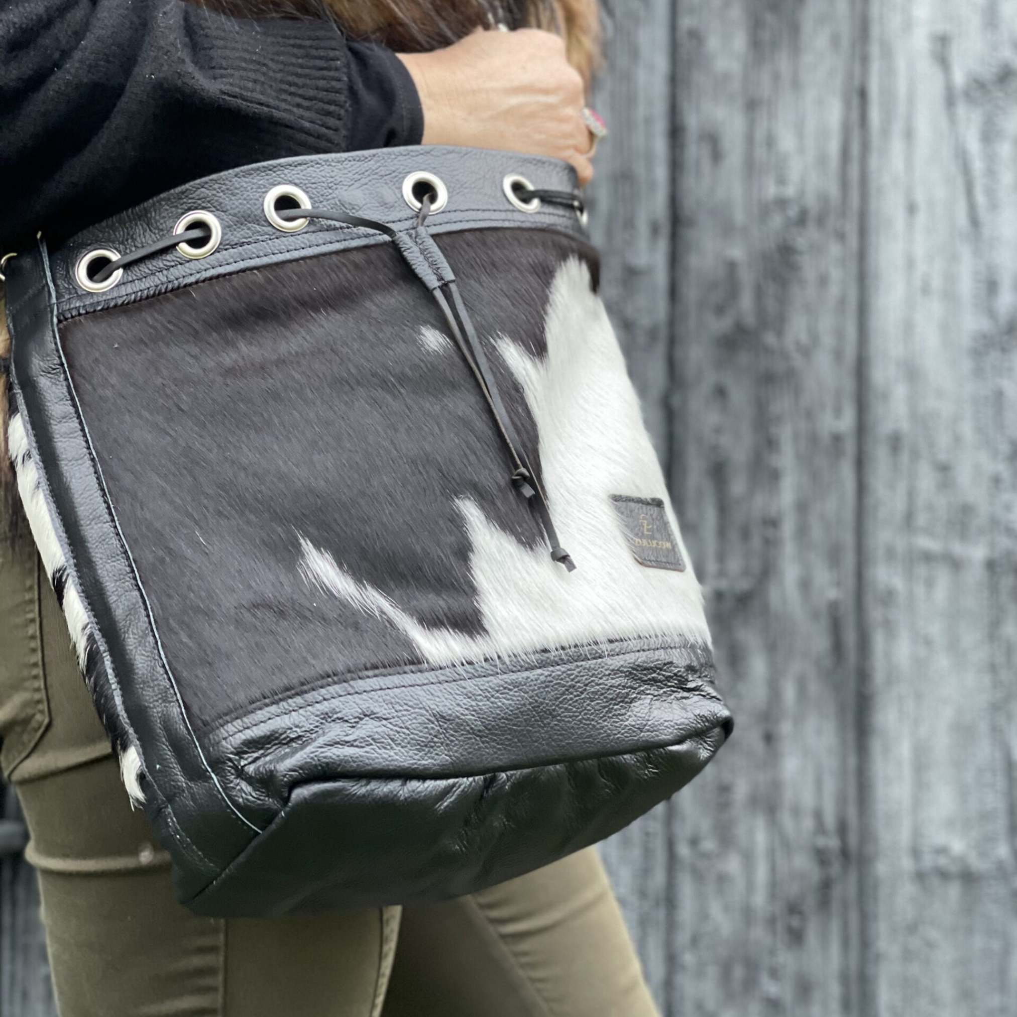 Close-up of a woman leaning against a wall with a black and white cowhide bucket bag slung over her shoulder