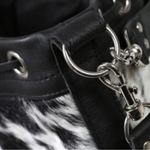 Close-up of a black and white cowhide bucket bag, highlighting the silver clasp and buckle details