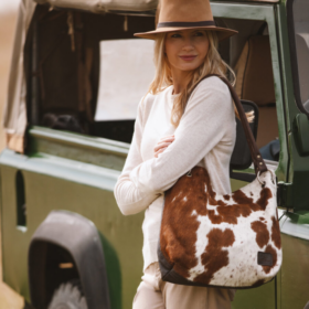 Woman wearing a brown and white cowhide slouch bag paired with a western boho style outfit, embracing a relaxed, stylish look