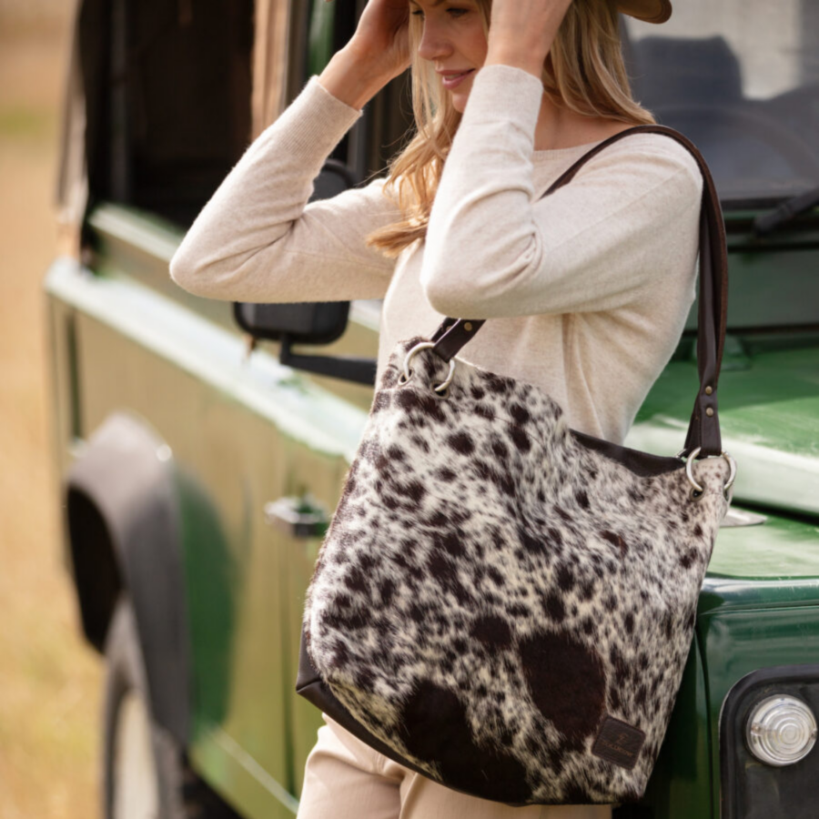 Woman wearing a brown and white cowhide slouch bag paired with a western boho style outfit, embracing a relaxed, stylish look