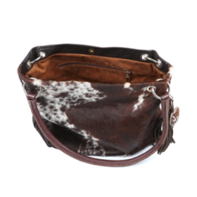 Close-up view of the interior of a brown and white cowhide slouch bag, featuring a spacious suede-lined compartment and zip pocket