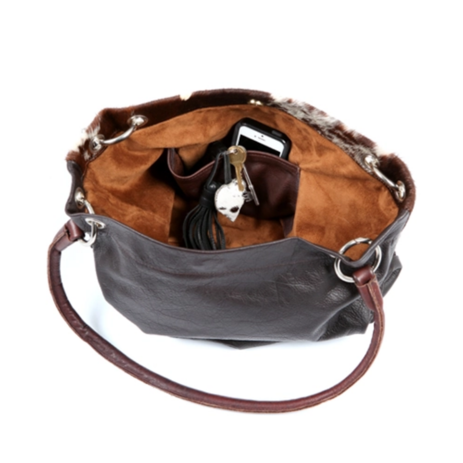 Close-up view of the interior of a brown and white cowhide slouch bag, featuring a spacious suede-lined compartment and zip pocket