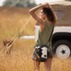 Woman standing in a field wearing a black and white cowhide bucket bag, with the bag slung over her shoulder