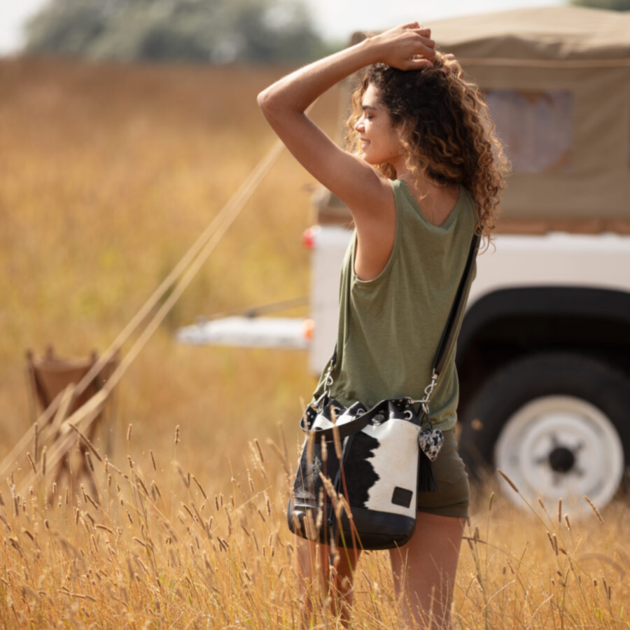 Woman standing in a field wearing a black and white cowhide bucket bag, with the bag slung over her shoulder