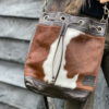 Close-up of a woman leaning against a wall while wearing a brown and white cowhide bucket bag