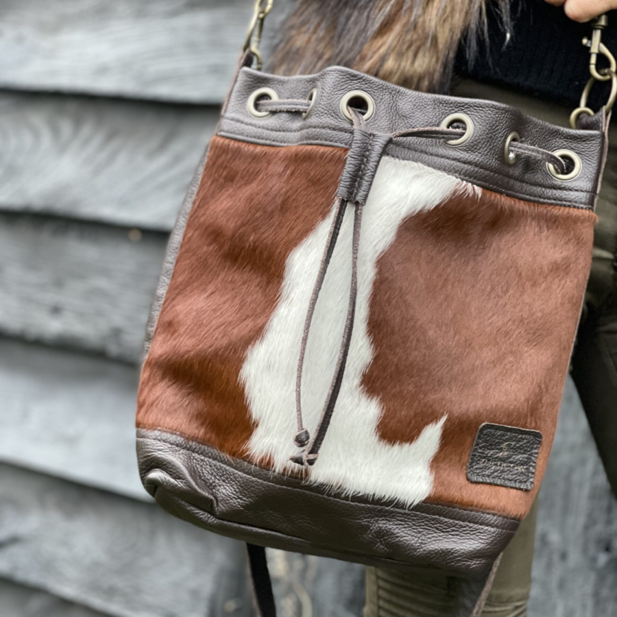 Close-up of a woman leaning against a wall while wearing a brown and white cowhide bucket bag