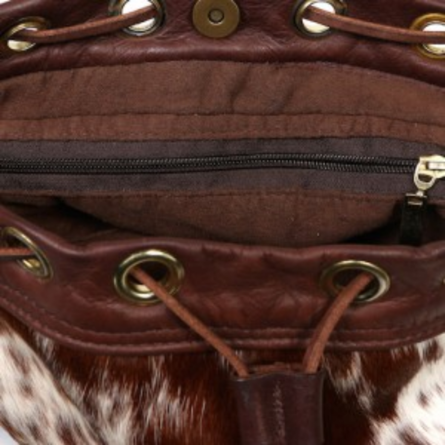 Close-up of the interior of a brown cowhide bucket bag, showing the zip pocket and leather drawstring closure