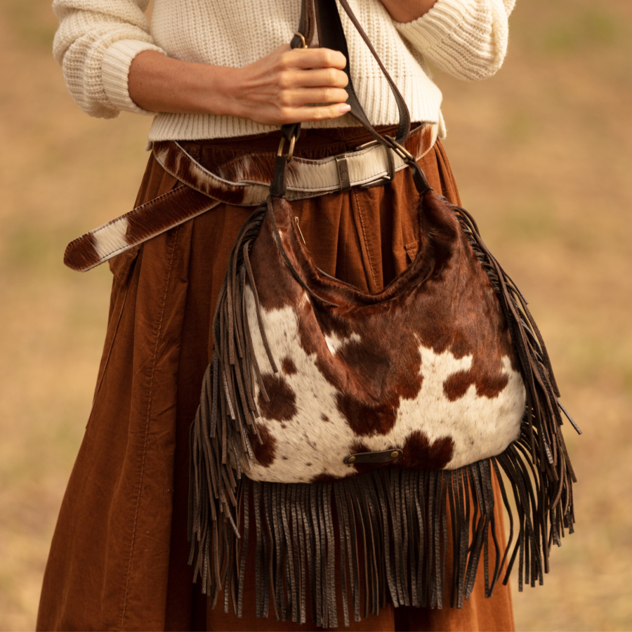 Woman wearing a boho Western style cowhide fringe bag, showcasing the fluid leather fringe and unique cowhide markings, with a relaxed, stylish outfit