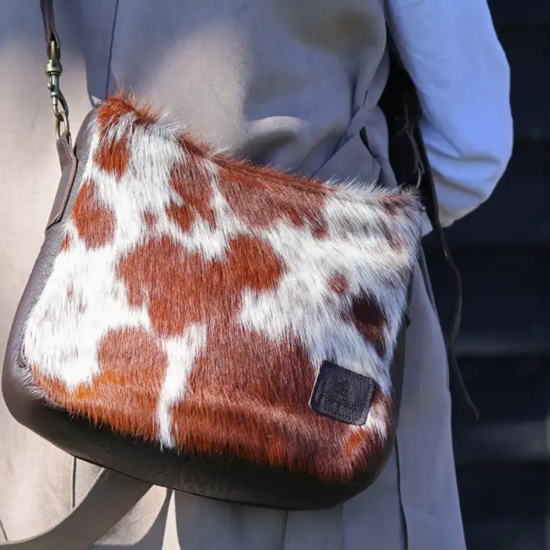 Woman wearing a stylish outfit with a brown and white cowhide saddle bag, featuring a sleek leather strap and unique Nguni cowhide pattern