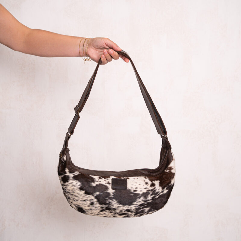 Chocolate brown and white cowhide sling bag with an adjustable leather strap, featuring a distinctive Nguni cowhide pattern