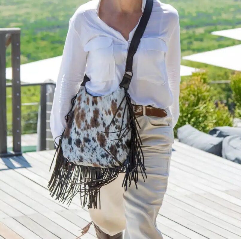 Woman wearing a boho outfit with a fringe cowhide bag, highlighting the natural texture and fringe details of the bag