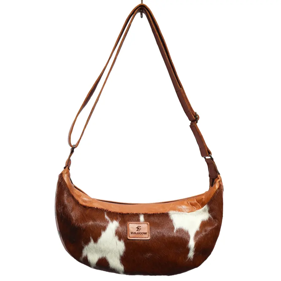 Ethically made cow print cowhide sling bag with adjustable leather strap and top zip closure
