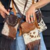 A woman wears 3 cowhide mini phone bags in various shades of brown, ranging from dark to light