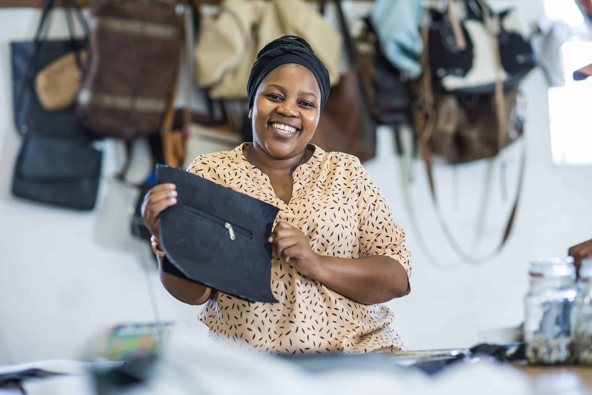 Khetiwe, a Zulu artisan woman, smiles whilst holding up the beginnings of a cowhide bag
