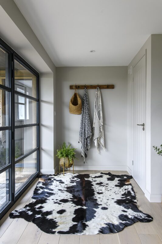A dark brown and white cowhide rug in a stylish sage green hallway