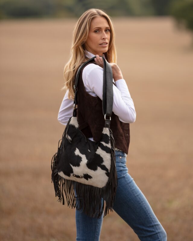 A model poses with a black and white cowhide fringe bag