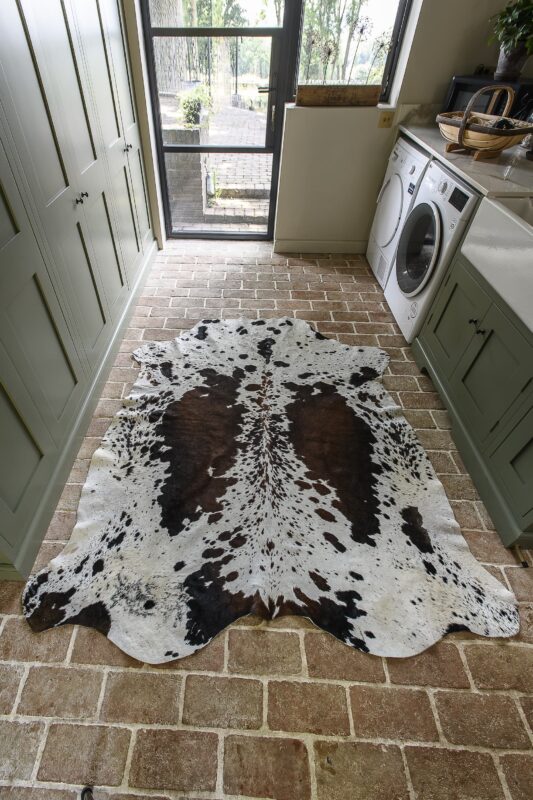 A brown and white rug on the stone floor of a sage green utility room